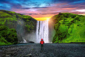 Skogafoss waterfall in Iceland. Guy in red jacket looks at Skoga devis-fall